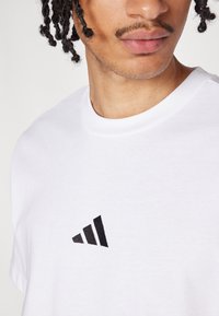 Λευκό βαμβακερό t-shirt με μαύρο κεντητό λογότυπο Adidas στην αριστερή πλευρά του στήθους, με στρογγυλή κοπή λαιμού και κοντά μανίκια.