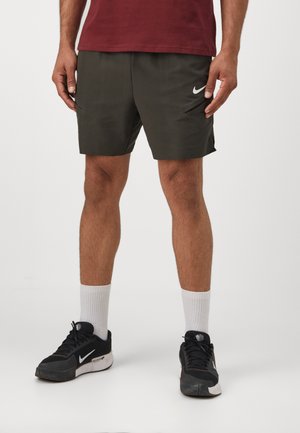 Șorturi atletice Nike de culoare verde închis, cu buzunare laterale și un material ușor. Asortați cu adidași negri și șosete albe.