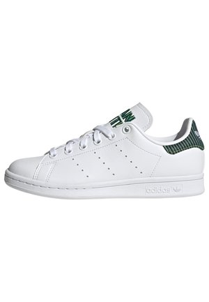 Weißer Sneaker mit niedrigem Schaft, weißen Schnürsenkeln, perforierten Seitendetails sowie dunkelgrünem, geripptem Fersenlaschen- und Zungenetikett.