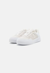Sneaker bianche con tomaia in tessuto testurizzato, accenti lisci bianchi a contrasto e suola in gomma spessa. Lacci e dettagli del logo visibili.