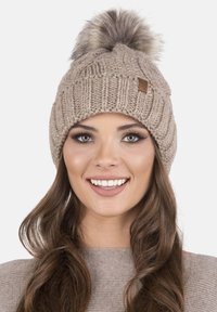 Berretto lavorato a maglia color camel con un motivo testurizzato e un grande pompon in finto pelliccia sulla sommità. Presenta un piccolo tag in pelle marrone sul lato.