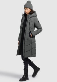 Doudoune grise avec capuche, fermeture éclair à l'avant et design matelassé en chevrons. Associée à un jean skinny noir et des bottines ; bonnet gris à côtes.
