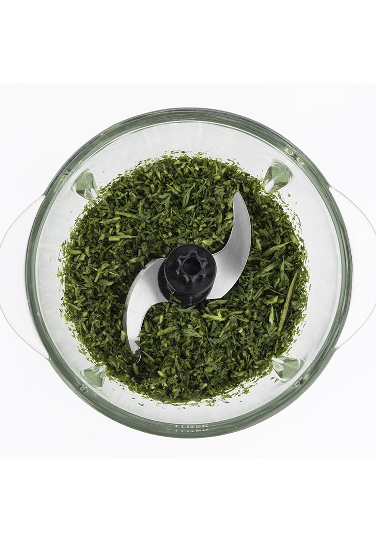 Tazón de procesador de alimentos de vidrio que contiene hierbas verdes finamente picadas, con una cuchilla de acero inoxidable en el centro y dos asas ergonómicas.