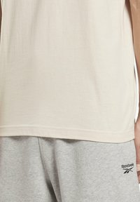 Beige bomulls T-shirt med korta ärmar, med en rund halsringning och en subtil textur. Matchas med ljusgrå sweatpants med en logotyp.