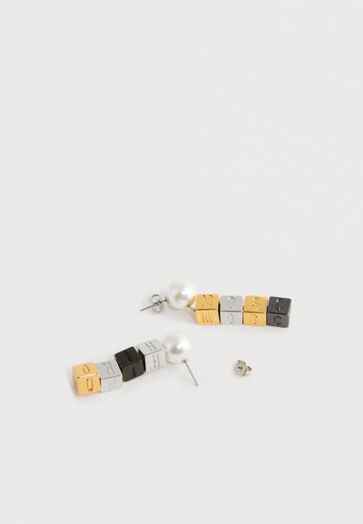 Paire de boucles d'oreilles en forme de cubes colorés formant le mot « MOSCHINO » avec des clous en perle sur fond blanc.