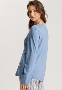 Camiseta de manga larga azul claro, hecha de algodón suave, con un cuello redondo y aberturas laterales en el dobladillo para facilitar el movimiento.