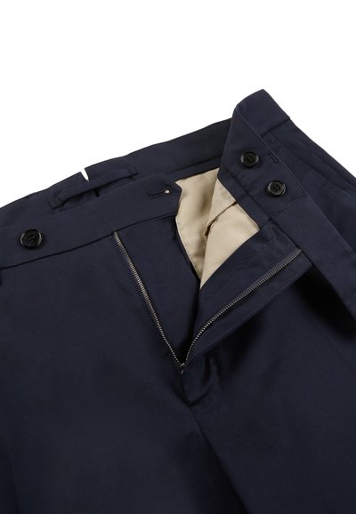 Pantaloni blu navy con cerniera parzialmente aperta, fodera interna beige visibile e bottoni neri in vita.