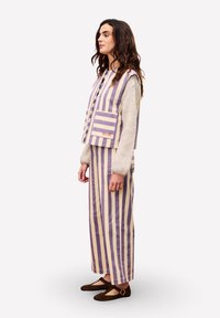 Gestreifter Weste in Lavendel und Creme mit Vorderaschen, kombiniert mit einem passenden langen Rock. Weicher Stoff mit lockerer Passform. Braune flache Schuhe.