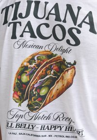 White t-shirt featuring a colorful graphic of two tacos filled with vegetables, accompanied by bold text reading "TIJUANA TACOS Mexican Delight".
