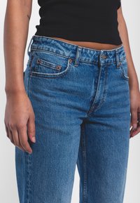 Jeans in denim azzurro chiaro con vita alta, caratterizzati da tasche frontali, accessori in rame e una texture leggermente sbiadita.