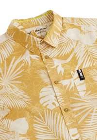 Korte mouwen shirt in mosterdgele stof met witte tropische bladenpatronen; voorzien van een kraag, knopenlijst en een borstzak met merklogo.