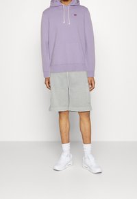 Felpa con cappuccio viola dotata di tasca frontale, abbinata a pantaloni corti grigi e sneakers bianche. Design semplice, materiale in cotone e colori neutri.