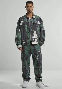 Multicolored denim jacket and cargo pants in green, black, and white diamond pattern. Features front pockets and drawstring cuffs.