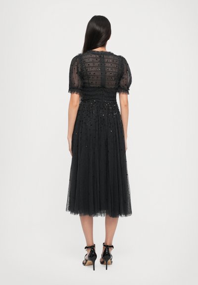 Zwarte tule jurk met een gestructureerde lijfje en pofmouwen. Bevat verspreide versieringen en een getailleerde taille, die tot een halflange zoom valt.
