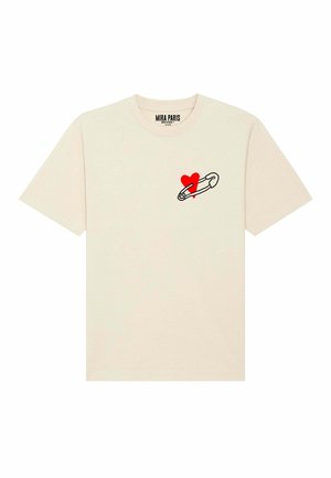 T-shirt en coton crème avec un contour noir d'une épingle de sûreté tenant un cœur rouge sur la zone gauche de la poitrine. Manches courtes, col rond.