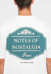 White t-shirt featuring a large teal graphic on the back with the text “NOTES OF NOSTALGIA” and “DON'T WASTE CULTURE” in black.