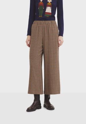 Pantaloni a quadri marroni e beige a gamba larga con vita elasticizzata, abbinati a stivali alla caviglia in pelle scura.