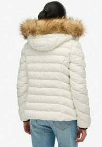 Hvid dunjakke med hætte og brun pelskant. Har quiltede sektioner og en afslappet pasform, kombineret med lyseblå jeans.