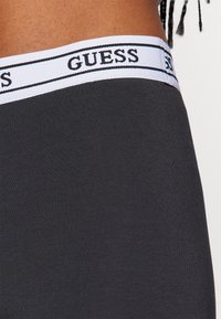 Boxers en coton noir avec une ceinture élastique blanche portant le nom de la marque "GUESS" en noir. Texture lisse, design ajusté.