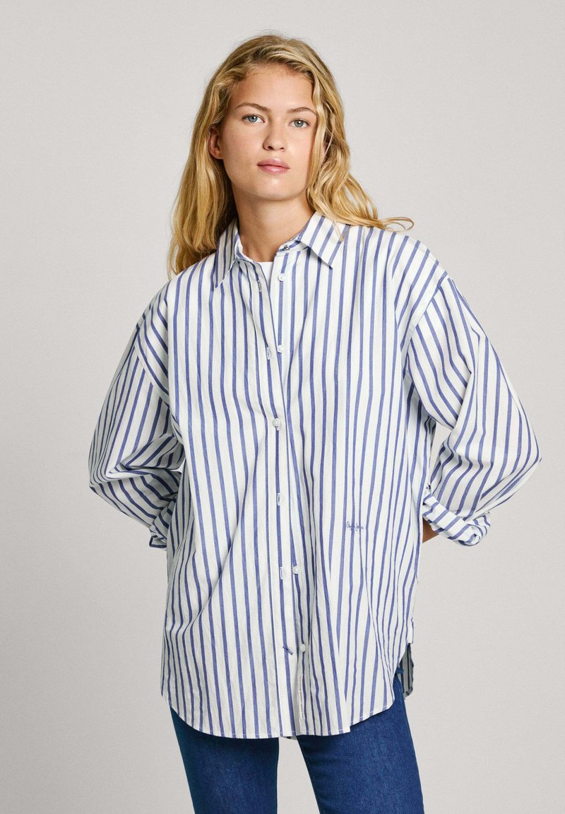 Camicia a righe bianca e blu. Presenta un colletto, maniche lunghe e una vestibilità rilassata. Il tessuto appare leggero con una consistenza liscia.