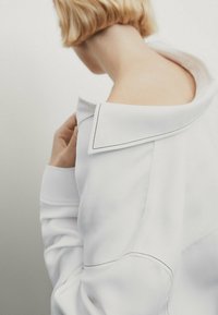 Maglione bianco oversize realizzato in morbido materiale, caratterizzato da un ampio colletto con cuciture nere a contrasto e una vestibilità comoda.
