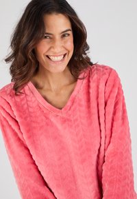 Fleece pullover in felle roze met een V-hals, gestructureerd chevronpatroon en lange mouwen met een accentsteek langs de halslijn.