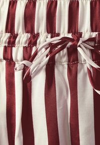 Röd- och vitrandig tyg med resårmidja och snörning. Mjuk struktur med synliga sömmar.