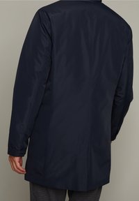 Abrigo impermeable azul marino con textura suave, mangas largas y corte recto. Presenta un diseño minimalista y costuras detalladas en las uniones.