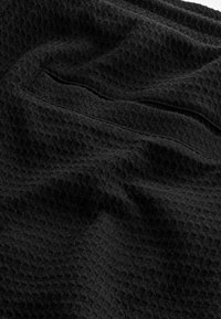 Tissu noir texturé avec un motif en gaufre, mettant en valeur des dimensions de surface variées et une apparence douce et tissée.
