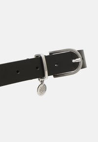 Cinturón de cuero negro con una hebilla de metal plateada, un lazo metálico y un charm con la letra "B". Textura suave, diseño minimalista.