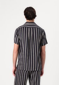 Camicetta a maniche corte di colore blu navy con strisce crema verticali, colletto classico e design con piega sul retro. Tessuto morbido con una vestibilità rilassata.