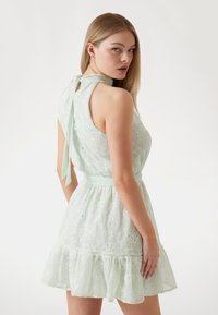 Mint green dress made of embroidered fabric, featuring a ruffled hemline, sleeveless design, and a tie closure at the back.