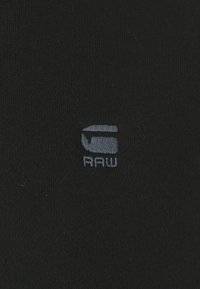 Tessuto nero con una superficie liscia, caratterizzato da un piccolo logo grigio in rilievo sul fronte che recita "RAW."