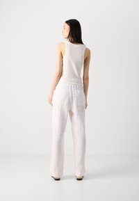 Débardeur blanc à coupe classique associé à un pantalon en lin beige clair ample, comportant une poche arrière et des jambes légèrement évasées.