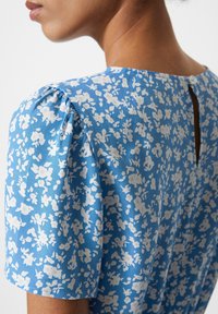 Blå blommönstrad klänning med korta puffärmar. Har en nyckelhålsöppning i ryggen och en slät tygtextur.