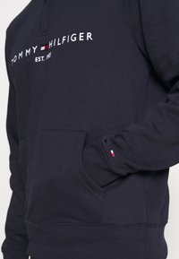 Sudadera azul marino de tejido suave con un bolsillo frontal, puños de canalé y el logo impreso de "TOMMY HILFIGER" con el año de fundación.