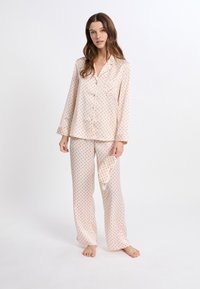 Conjunto de pijama de satén rosa claro con lunares rojos. Camisa de botones de manga larga y pantalones a juego con una textura suave. Incluye una máscara de sueño a juego.
