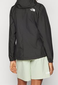 Mustat hupparitakki, jossa on joustavat hihansuut ja logo selässä. Yhdistetty vaaleanvihreisiin shortseihin, jotka näyttävät sileiltä ja matalta.