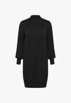 Abito nero con scollatura rotonda alta, maniche in maglia testurizzata e polsini aderenti. Il corpo è liscio, creando una silhouette moderna.
