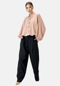 Blusa rosa chiaro con colletto e chiusura a bottoni, con maniche voluminose. Abbinata a pantaloni neri a vita alta e tacchi nudi.