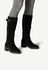 Stivali alti fino al ginocchio in suede nero con tacco a blocco, zip laterale e dettaglio con fibbia sul polpaccio; presentano accenti di cucitura per una maggiore texture.