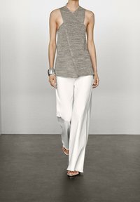 Haut sans manches en maille grise avec décolleté en V et design croisé ; associé à un pantalon blanc à jambes larges et à des sandales argentées à bout ouvert.