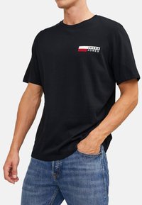 Schwarzes Baumwoll-T-Shirt mit kleinem weißen, roten und blauen Logo auf der Brust, kurzen Ärmeln und lockerer Passform.