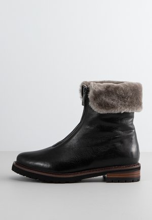 Botín negro de cuero con un suave collar de piel sintética gris. Cuenta con un cierre lateral y una suela de goma texturizada con un acento de madera.