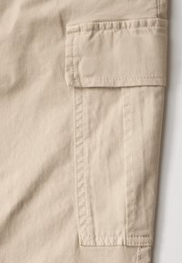 Béžové cargo kalhoty s boční kapsou, vyrobené z texturované bavlněné látky s viditelným prošíváním a hladkým povrchem.