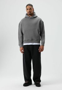 Grijze capuchonsweater met voorspocket, losse pasvorm, geribbelde manchetten, gecombineerd met zwarte losse jeans en zwarte schoenen.