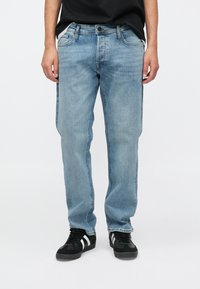 Lichtblauwe denim jeans met een recht model, vijf zakken en subtiele vervaging. Gecombineerd met zwarte sneakers met witte strepen.