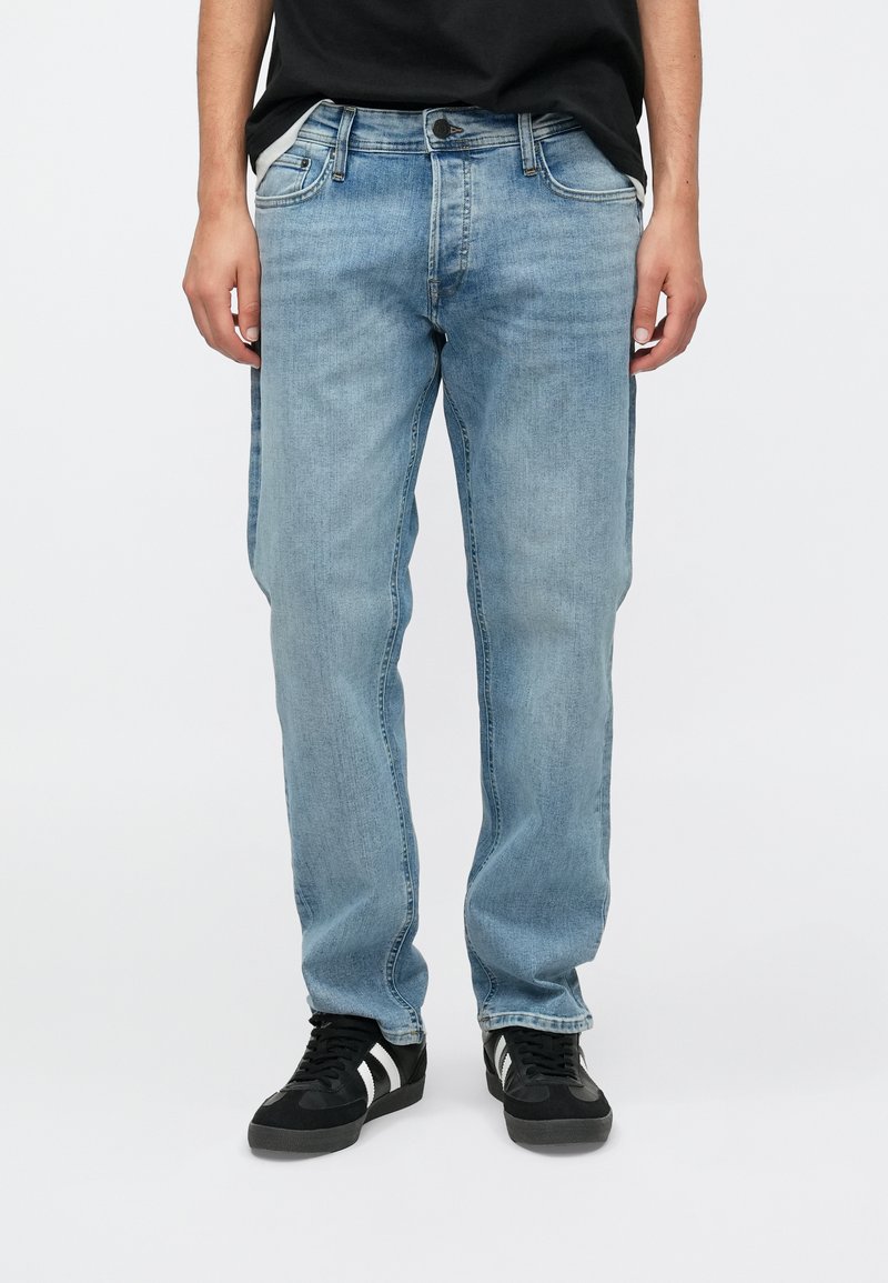 Lichtblauwe denim jeans met een recht model, vijf zakken en subtiele vervaging. Gecombineerd met zwarte sneakers met witte strepen.