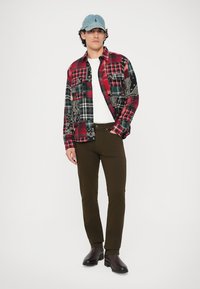 Rød og svart rutete flanellskjorte med bandana-mønstre, hvit t-skjorte med rund hals, olivengrønne bukser og mørke støvler, toppet med en blå denimlue.