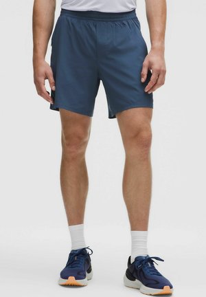 Shorts negri de bărbați, dintr-un material ușor, cu talie elastică și buzunare laterale. Combinat cu adidași negri și șosete albe.